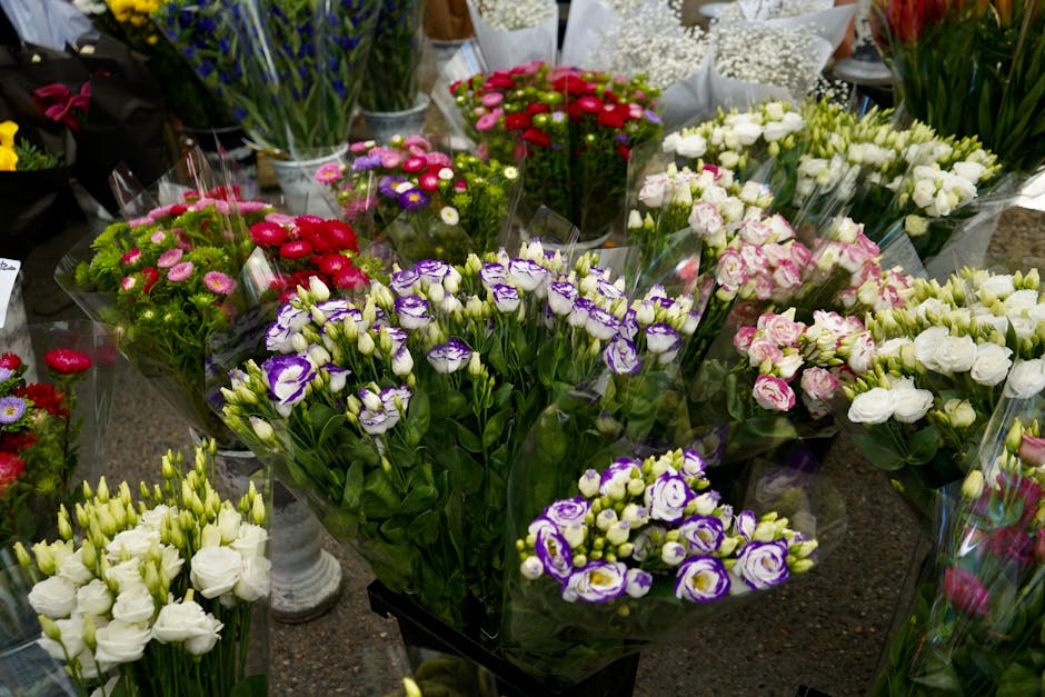A vibrant display of freshly arranged flower bouquets at a florist shop, featuring an array of colors including white, pink, purple, and red. The bouquets, wrapped in clear cellophane, consist of vari