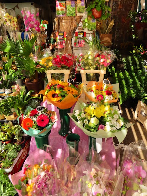 A display of fresh flower bouquets arranged on black metal stands and a table inside a flower shop, featuring vibrant blooms such as red gerbera daisies, yellow chrysanthemums, and white roses, wrappe
