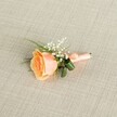 A delicately crafted peach rose boutonniere lies horizontally on a softly textured light beige linen background, its fine weave running evenly beneath the flowers like a calm, neutral canvas. At the heart of the design is a single rose in a warm peach shade, partially open so that its petals gently curl back from a creamy outer edge into a deeper apricot and soft orange glow at the centre, as if just cut fresh from a garden in South Croydon. Nestled to the upper right of the bloom, airy clusters of white baby's breath (gypsophila) add a cloud-like lightness, each tiny blossom catching the soft, even lighting and creating a gentle contrast against the rose's fuller form. Fine, grass-like green sprigs extend from behind the flowers, offering a lively splash of colour, while two broader, darker green leaves curve protectively around the base, lending structure and depth. The stems are neatly bound in a matte peach satin ribbon, wrapped with care and finished in a small, graceful bow that suggests the patient hands of an experienced local florist preparing it for a wedding near Croham Hurst or a prom at a nearby South Croydon school. The lighting is calm and diffused, enhancing the satin sheen of the ribbon, the velvety rose petals, and the woven fabric beneath, giving the whole scene a quietly celebratory feel. This boutonniere looks ready to be pinned to a lapel for a special occasion, capturing the tenderness of a romantic celebration, whether it's a registry office ceremony on Brighton Road or a family gathering just off Selsdon Road, where simple, refined flowers say more than words.
