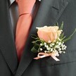 There's a quiet, resplendent beauty woven into this classic boutonniere, so often seen gracing formal attire during weddings and celebrations in South Croydon. Focal to the arrangement is a singular, gently blooming peach rose, its petals buttery-soft and arrayed in harmonious spirals, capturing the fleeting blush of dawn that can be glimpsed at Wandle Park. Wisps of white baby's breath encircle the rose, their airy appearance conjuring the purity and hopeful energy of new beginnings. Slender trimmings of fresh, green foliage twist and curl alongside a deeper green leaf, echoing the lushness of South Croydon's parks and gardens. The composition is thoughtfully completed by a petite bow of peach satin ribbon at the boutonniere's base, its gleam mirroring the warm note of a silk tie tucked neatly under a crisp, light blue checked shirt. The overall effect is polished yet heartfelt-a subtle, fragrant tribute to love, celebration, and connection. Crafted with expert care, these buttonholes are more than accessories; they are tokens that flutter at the heart of a South Croydon event, carrying with them a hushed fragrance and shimmering promise, designed to be delivered fresh for moments you'll cherish.