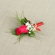 A single rose boutonniere in rich crimson-red tones lies diagonally across a softly textured, light beige fabric, the neutral background similar to natural linen and reminiscent of the classic textiles you might find in a South Croydon bridal studio. At the centre, a tightly furled rosebud glows in deep crimson with a hint of fuchsia, each velvety petal wrapped closely around the next, giving the flower a sense of poised anticipation, as if about to open just in time for a wedding ceremony at nearby Croydon Minster. Clusters of tiny white baby's breath nestle around the rose, their cloud-like blooms adding lightness and a gentle contrast, like small puffs of mist surrounding a sunset. Behind and around these blooms, fresh green foliage stretches outward: a few broader, darker leaves form a sturdy base, while slender, grass-like, bright green sprigs splay delicately, bringing movement and an airy texture that frames the central rose without overpowering it. The stems are neatly gathered and wrapped in a rich red satin ribbon, its glossy surface catching the light in subtle highlights, wound tightly and finished with a neat loop or small bow that hints at careful, practiced hands. The lighting is bright yet soft, enhancing the rose's velvety texture and the crisp whiteness of the gypsophila, making the whole boutonniere feel freshly made, as though it has just been prepared for a groom's lapel before a celebration in one of South Croydon's intimate venues. This refined lapel flower conveys romance, elegance, and timeless style, perfect for weddings, proms, Valentine's Day dinners, or any formal event where a single, beautiful detail makes all the difference.