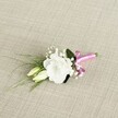 A delicately crafted wedding boutonniere is laid diagonally across a softly textured, oatmeal-beige fabric that looks like finely woven linen, its subtle threads catching the gentle, even light. At the heart of this petite design sits a single, fully opened white lisianthus blossom, its ruffled petals layered in soft curves that create a cloud-like, almost luminous centrepiece. Just beside it, two slender cream-and-pale-green lisianthus buds rest closely together, suggesting flowers that will unfurl later in the day, much like the unfolding moments of a ceremony in South Croydon. Tiny clusters of white gypsophila are threaded throughout, their airy, bead-like blooms adding a light, misty halo around the focal flower. Slim, grass-like blades of fresh green foliage arc gracefully towards the lower left, giving the piece a feeling of movement, as if a breeze from nearby Croham Hurst Woods had just brushed past. A broader, deeper green leaf is tucked quietly behind the main bloom, grounding the composition with a gentle, natural weight. At the base, the neatly aligned stems are bound with a bright fuchsia satin ribbon, tied into a small, precise bow that introduces a playful splash of colour against the neutral background. The sheen of the ribbon hints at a silky texture between the fingers and adds a modern, celebratory twist to this classic white-and-green palette. This intimate boutonniere, perfectly sized for a groom's or groomsman's lapel at a South Croydon registry office or local church, radiates quiet elegance, freshness, and the soft promise of a joyful day, captured in a single detailed, overhead image.