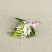 A delicately handcrafted floral boutonniere rests on a softly textured light beige fabric, similar to natural linen laid out on a dressing table in a South Croydon home before a special event. At the heart of the compact design is a single white alstroemeria, or Peruvian lily, its broad petals gently curved and slightly ruffled at the edges. Fine reddish-brown speckles gather near the throat of the bloom, drawing attention to the central stamens and creating a subtle, painterly detail. To the left, a tight conical spike of vivid lime green buds, likely Ornithogalum, adds striking structure and a modern twist with its neat, scale-like pattern. Around these focal elements, cloud-like sprigs of pure white baby's breath appear to float, softening the silhouette and giving the piece a light, airy feel. A base of dark green, pointed leaves anchors the composition, while slender, grass-like fronds weave through the flowers, adding movement and a whisper of wild garden energy, reminiscent of greenery along Croham Hurst or around South Croydon's quiet side streets. At the right, a glossy pastel pink satin ribbon is tied into a neat little bow, securing the stems and introducing a playful yet refined accent of colour. The light falls evenly over the arrangement, enhancing each texture-from the satin sheen of the ribbon to the velvety petals and crisp foliage. The overall impression is one of fresh, understated elegance, perfect for pinning to a lapel at a wedding near Lloyd Park, wearing to a prom, or marking a cherished anniversary celebration in South Croydon with a touch of gentle romance and careful craftsmanship.